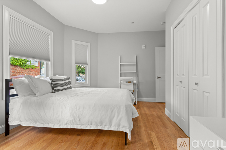 A bedroom with a bed, a window with a view of a brick wall, and a wooden floor.