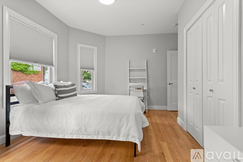 A bedroom with a bed, a window with a view of a brick wall, and a wooden floor.