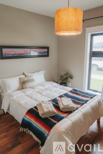 A bedroom with a bed covered in a white comforter and a colorful blanket.