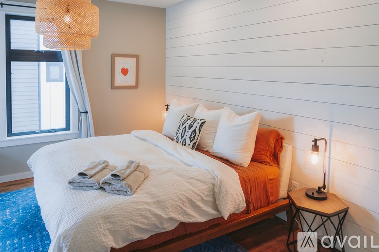 A bedroom with a bed, pillows, a lamp, and a picture on the wall.