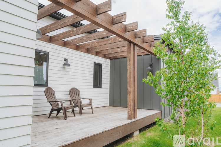 A wooden pergola is attached to a white house.