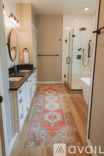 A bathroom with a rug on the floor and a shower with a glass door.