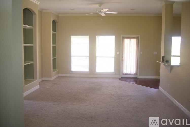 A room with a carpeted floor, a ceiling fan, and a window with white curtains.