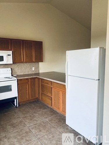 A kitchen with a white fridge, white stove and wooden cabinets.