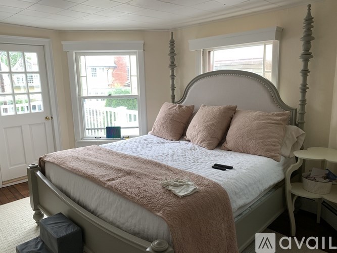 A bedroom with a large bed and a window overlooking a fence.