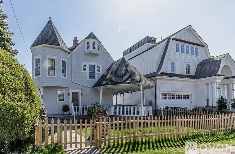 A white house with a black roof and a wooden fence in front.