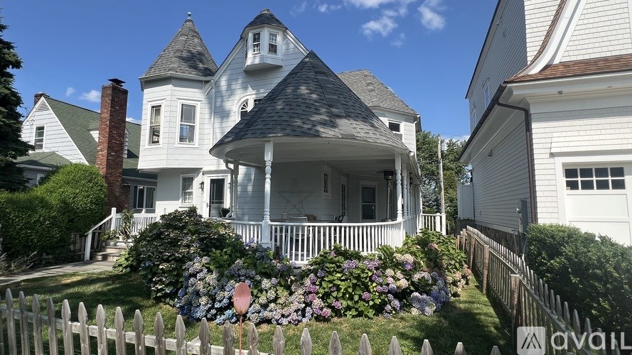 A white house with a turret and a porch surrounded by a white picket fence.