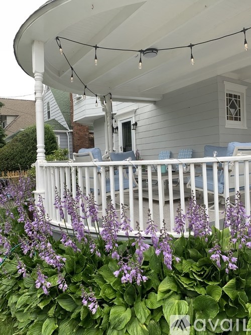 A white porch with a white railing and purple flowers in front.