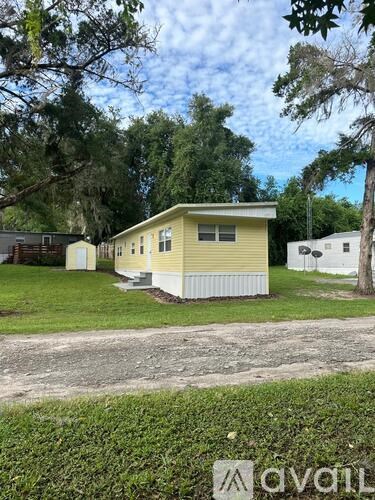 A yellow house with a white fence is surrounded by greenery.