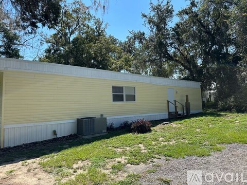 A yellow house with a white window and a door is surrounded by trees.