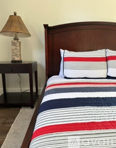 A bed with a striped comforter and pillows next to a lamp on a nightstand.