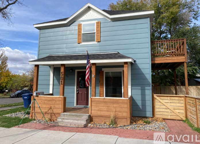 A blue house with a wooden deck and a flag on the front porch.