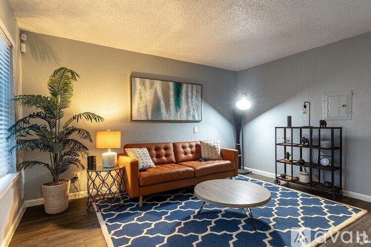 A living room with a brown couch, a blue rug, and a painting on the wall.