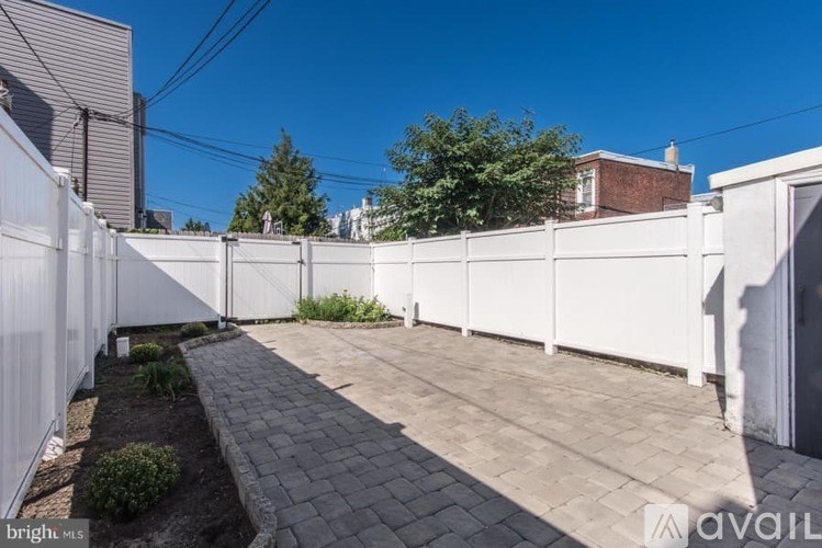 A backyard with a white fence and a brick pathway.
