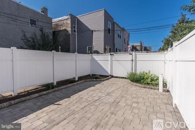 A white fence surrounds a brick patio in a sunny backyard.