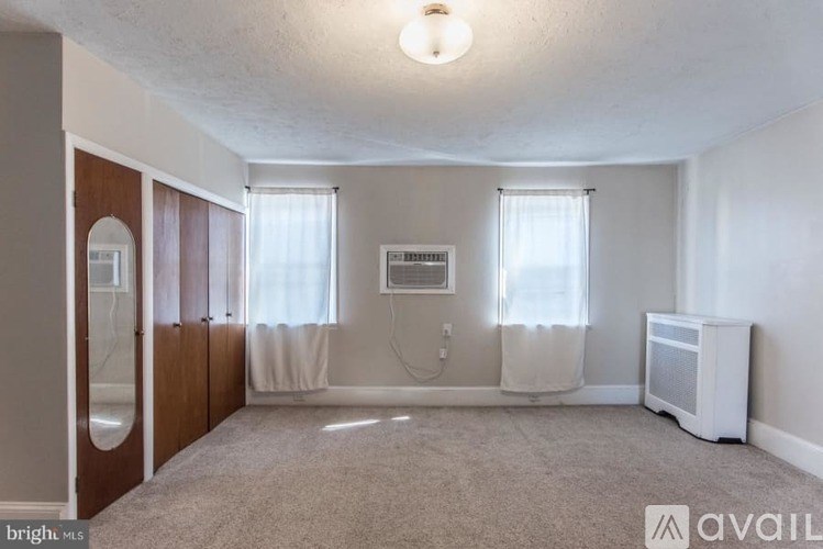 A room with a carpeted floor, a window with curtains, and a white air conditioning unit.