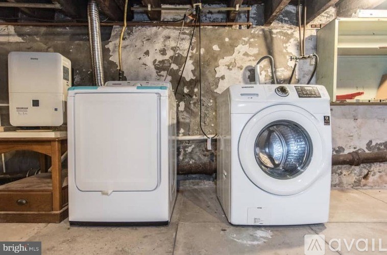 A white dryer and washer are sitting next to each other in a room with a dirty wall.