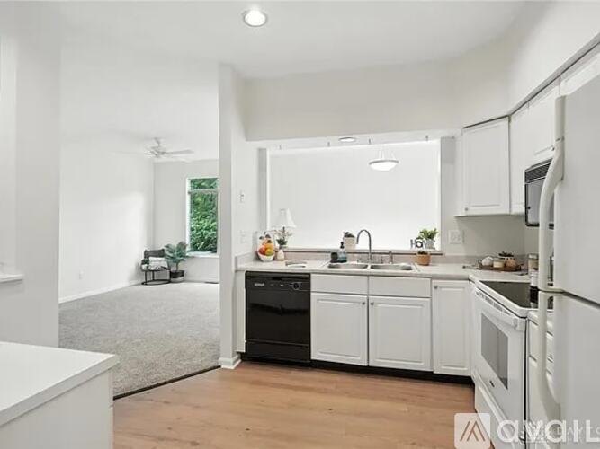 A modern kitchen with white cabinets and appliances, a grey rug, and a window with a view of greenery outside.