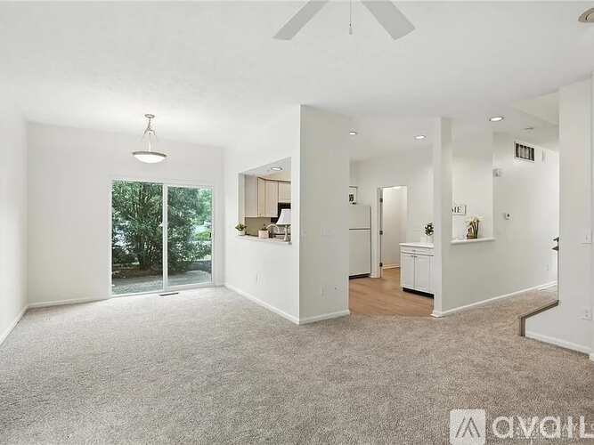 A spacious living room with a ceiling fan and carpeted floor.