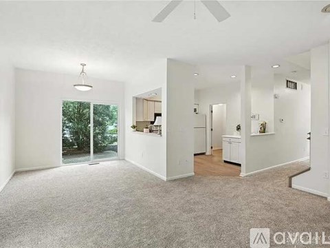 A spacious living room with a ceiling fan and carpeted floor.