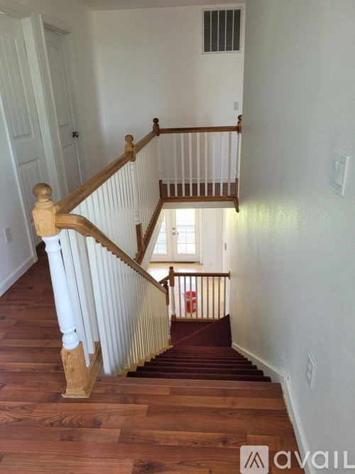 A wooden staircase with a white railing leads to a small landing with a window.