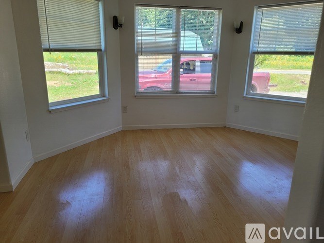A room with wooden floors and two windows overlooking a parking lot.