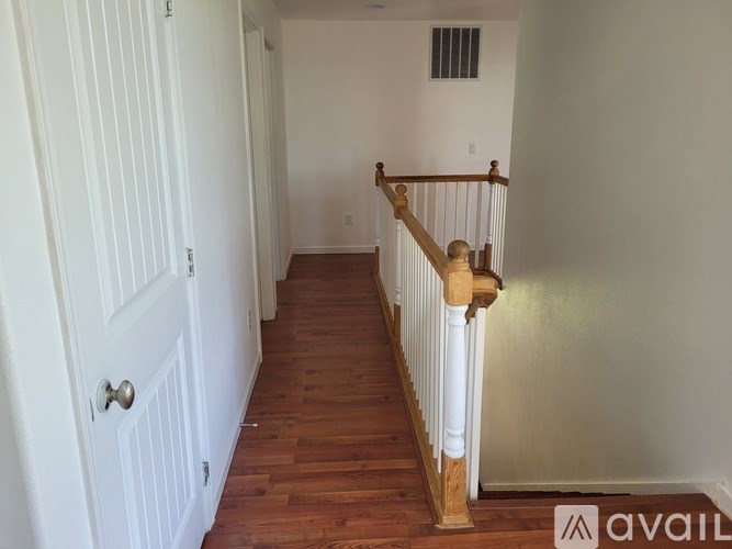 A hallway with a wooden floor and a white railing.