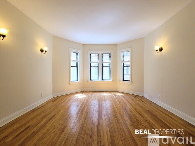 A spacious room with wooden floors and three windows.