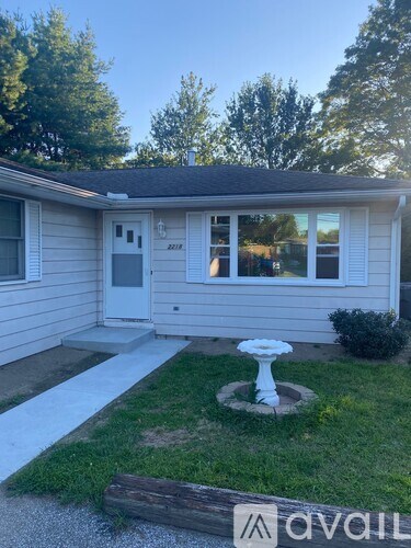 A small house with a white door and a white fountain in the front yard.