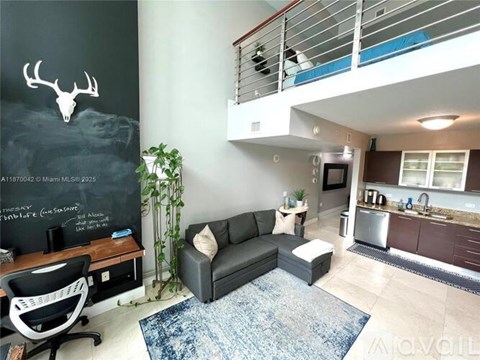 A living room with a black couch and a chalkboard wall with a deer head on it.
