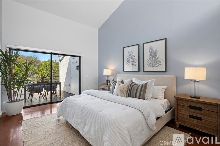 A bedroom with a large bed, two lamps, and a potted plant.