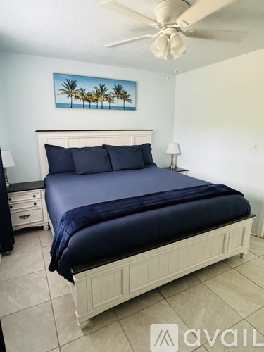 A bedroom with a bed, nightstand, and a painting of palm trees on the wall.