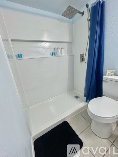 A white toilet sits under a blue shower curtain in a small bathroom.