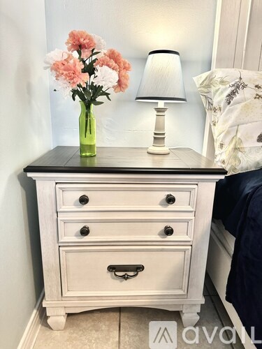 A white nightstand with a green vase of flowers on top.