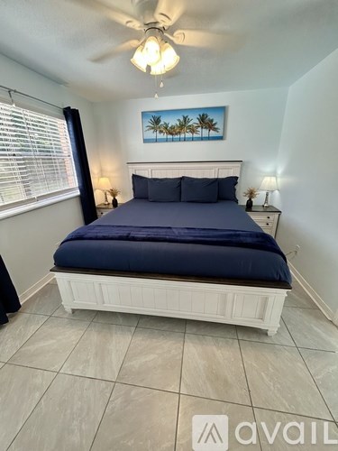 A bedroom with a bed, nightstands, and a painting of palm trees on the wall.