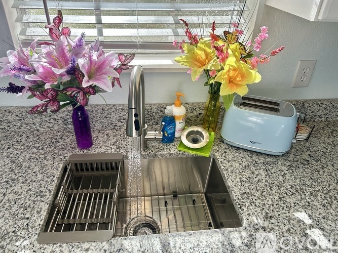 A kitchen sink with a silver faucet and a vase of flowers on the counter.