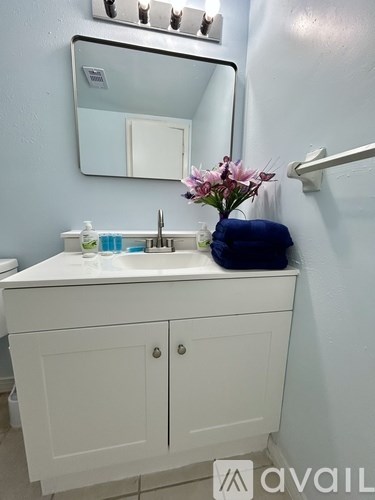 A white bathroom vanity with a sink, mirror, and a vase of flowers.