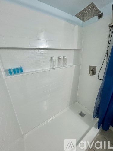 A white tiled shower with a blue shower curtain and a shelf above the tub.