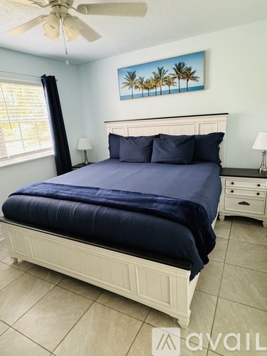 A bedroom with a large bed and a painting of palm trees on the wall.