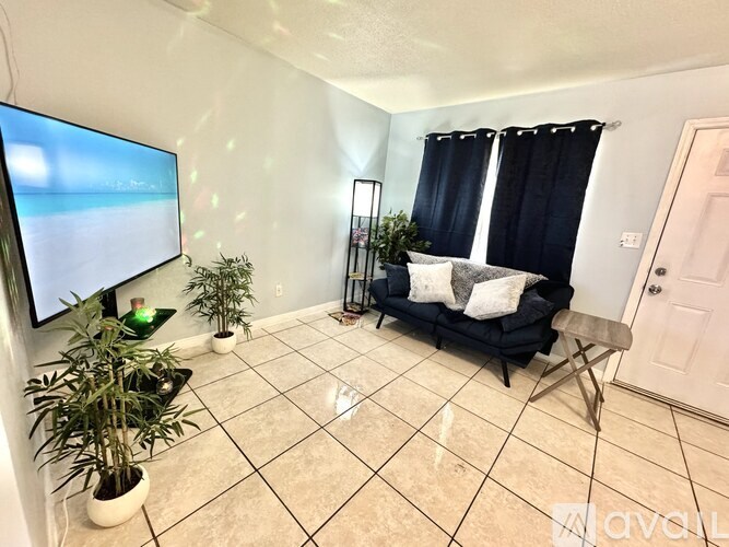 A living room with a flat screen TV, a black sofa, and a potted plant.