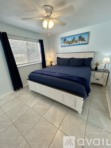 A bedroom with a bed, nightstand, and a painting of palm trees on the wall.