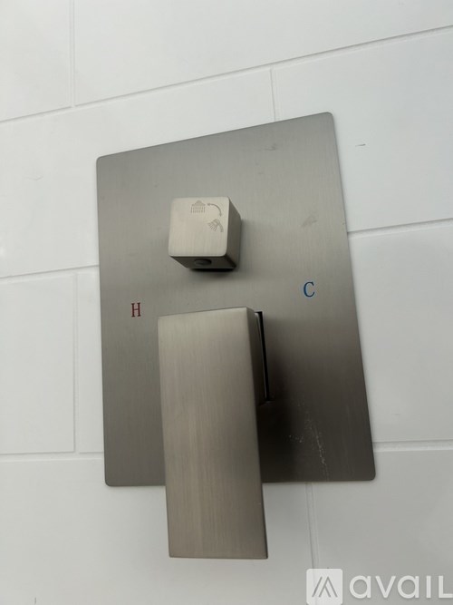 A wall-mounted thermostat with a white top and a grey bottom is mounted on a white wall.