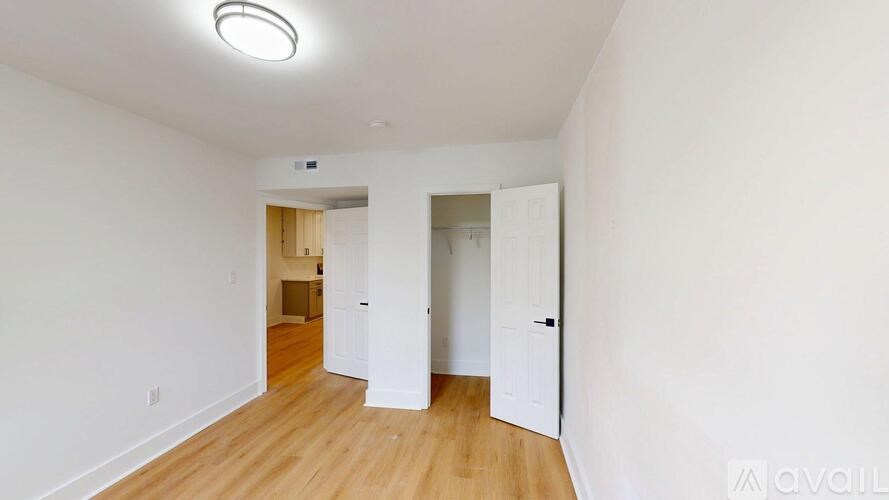 A room with wooden floors and white walls, with a doorway leading to another room.
