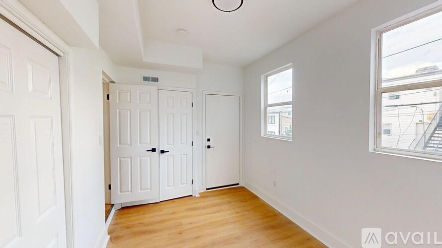 A room with white walls and wooden floors, featuring a white door and a window.