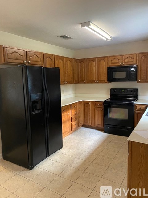 A black refrigerator stands in a kitchen with wooden cabinets.