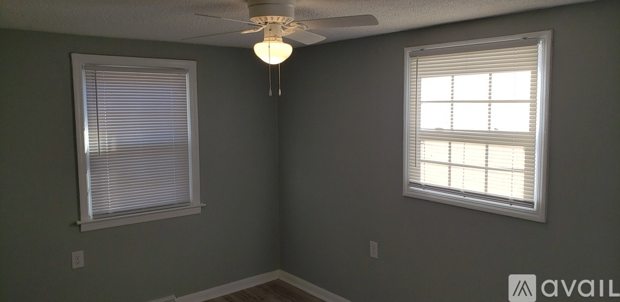 A room with a ceiling fan and two windows.