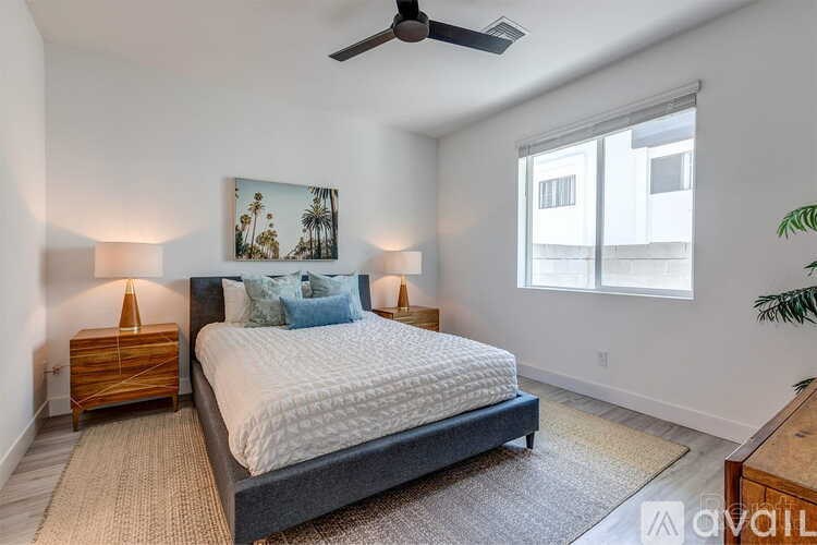 A bedroom with a large bed, a ceiling fan, and a painting of palm trees on the wall.