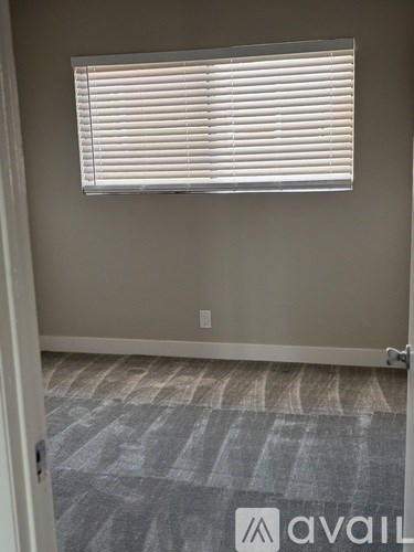 A room with a carpeted floor and a window with blinds.