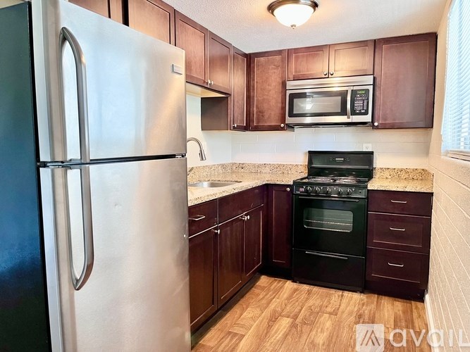 A kitchen with a stainless steel refrigerator, black oven, and wooden cabinets.