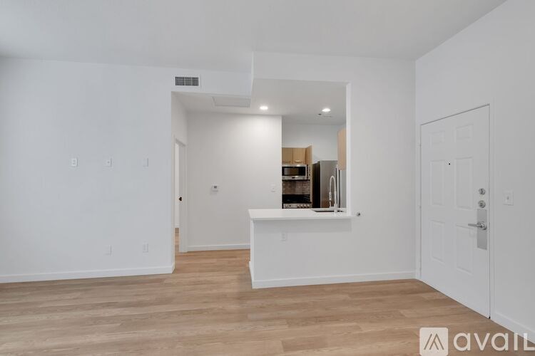 A room with white walls and wooden flooring, with a white counter and a white door on the right.